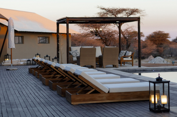 Otjiwa Thornbush Tented Camp: Pooldeck mit Holzliegen und Kerzenlaternen im Abendlicht