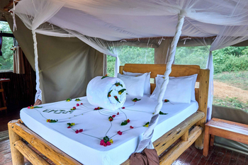 Migunga Tented Camp: Holzrahmenbett mit Blumenarrangement und Moskitonetz
