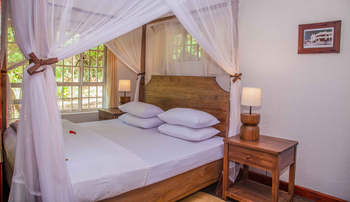 Moivaro Lodge: Holzbett mit Moskitonetz im Sonnenlicht