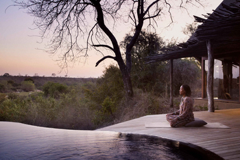 Singita Boulders Lodge: Meditierende Person auf Holzdeck bei Dämmerung