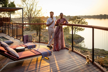Anantara Tented Camp Kafue River: Zwei Gäste bei goldenem Sundowner auf Flussdeck
