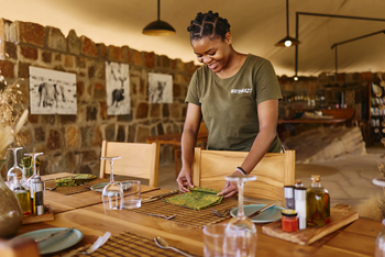 Mkomazi Wilderness Retreat: Mitarbeiterin deckt luxuriösen Speisetisch im Tageslicht.