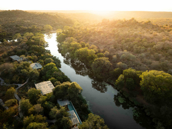 Singita Sweni Lodge: Holzstege über goldschimmerndem Buschfluss bei Dämmerung
