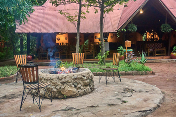 Migunga Tented Camp: Steinfeuerstelle und Holzstühle im Grünen