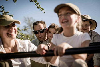 Singita Sweni Lodge: Familie lehnt am Safarifahrzeug unter klarer Mittagssonne
