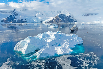 Antarktis: Schimmernder Eisberg mit Expeditionsbooten