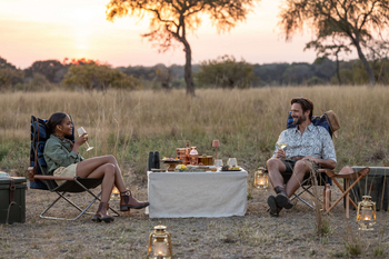 Anantara Tented Camp Kafue River: Zwei Gäste genießen Sundowner im goldenen Busch