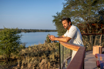 Anantara Tented Camp Kafue River: Gast mit Sundowner überblickt Fluss im Abendlicht