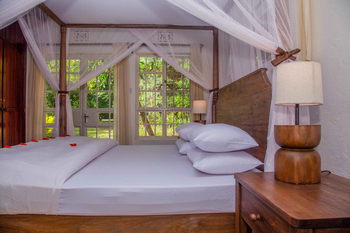 Moivaro Lodge: Großes Holzbett mit Moskitonetz und Blütenblättern