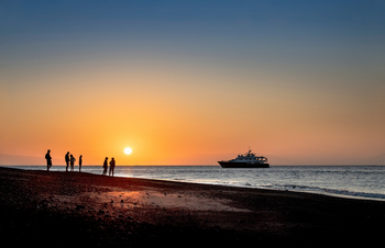 andBeyond Galapagos Explorer: Gäste beobachten goldenen Sonnenuntergang am Küstenstrand
