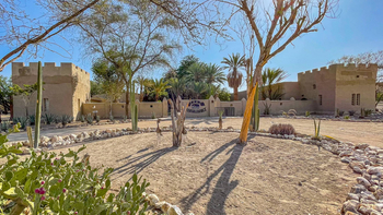 Fort Sesfontein Lodge: Steinschild Sesfontein flankiert von hohen Kakteen