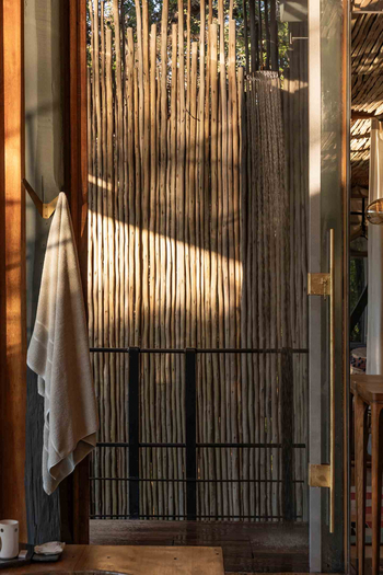 Singita Sweni Lodge: Freiluftdusche zwischen Holzpfählen im Morgenlicht