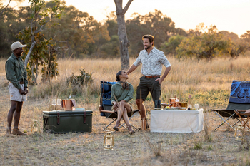 Anantara Tented Camp Kafue River: Drei Gäste bei Sundowner im goldenen Busch