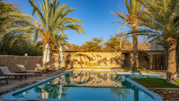Fort Sesfontein Lodge: Pool mit Safari-Wandbild und Palmen