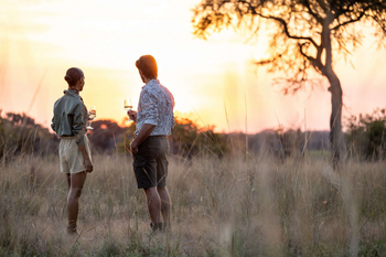 Anantara Tented Camp Kafue River: Zwei Gäste beim Sundowner auf weiter Savanne