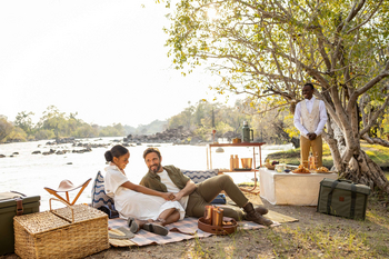 Anantara Tented Camp Kafue River: Zwei Gäste beim Sundowner-Flusspicknick mit Butler