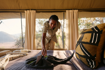 Mkomazi Wilderness Retreat: Mitarbeiterin bereitet Zeltbett bei goldenem Licht.