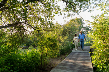 Singita Lebombo Lodge: Paar spaziert Holzsteg entlang im grünen Busch