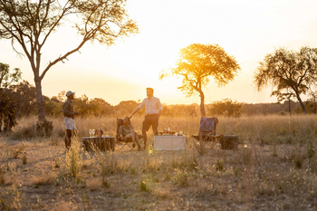 Anantara Tented Camp Kafue River: Drei Gäste beim Sundowner im goldenen Busch