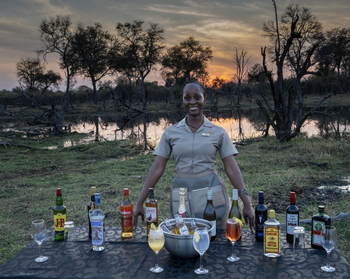 Losika Elephant Camp: Lachende Mitarbeiterin an Sundowner-Bar unter Abendrot
